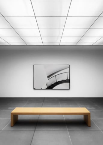 A wooden bench overlooking a large abstract painting on the wall.