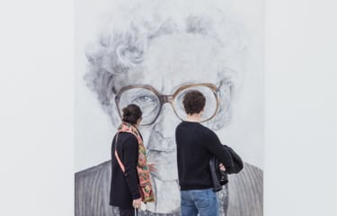 two museum visitors looking at a giant black and white portrait of an older lady